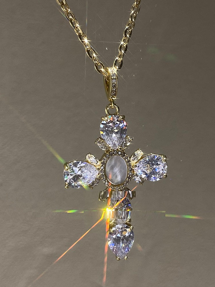 Gold cross pendant with clear gemstones on a reflective surface