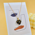 Necklace with a heart-shaped pendant on a card with abstract designs, against a yellow background.