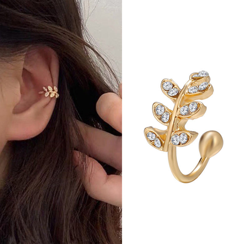 Gold leaf-shaped earring worn on an ear with a close-up of the earring on a white background.