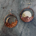 Copper earrings with moon and crescent designs on a stone surface