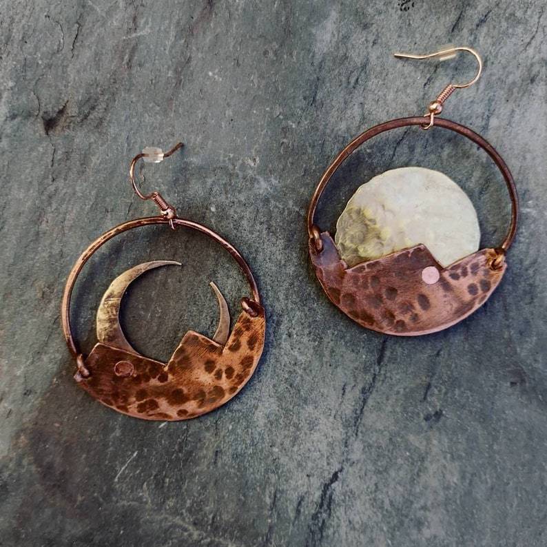 Copper earrings with moon and crescent designs on a stone surface