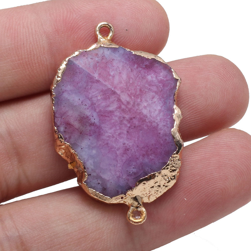 Purple stone pendant with gold edge held between fingers on a white background