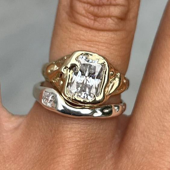 Gold ring with a large diamond on a finger against a neutral background