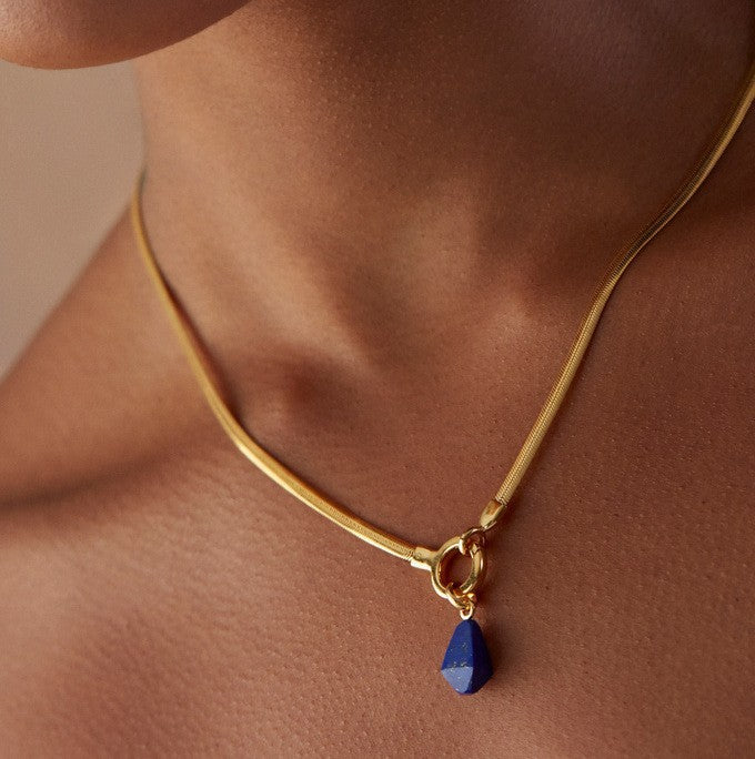 Gold necklace with a blue pendant on a person's neck against a neutral background