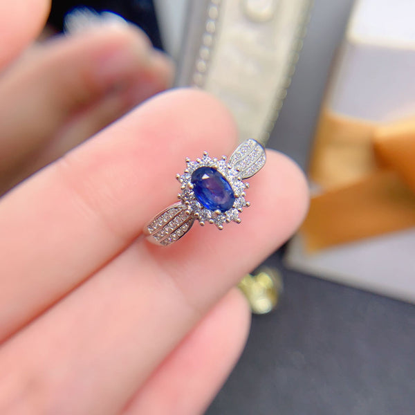Silver ring with a blue gemstone held on a finger against a blurred background