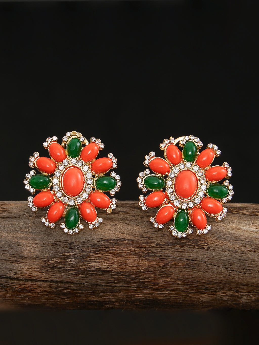 Pair of floral earrings with orange and green stones on a dark surface