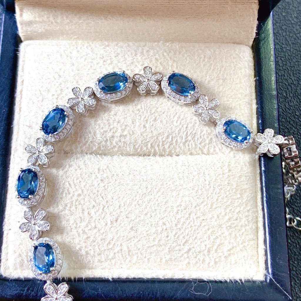 Bracelet with blue gemstones and floral designs on a white cushion in a jewelry box.