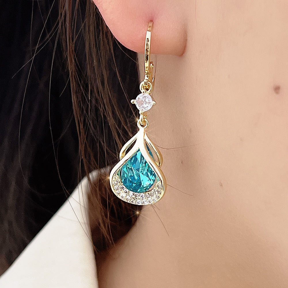 Gold earring with blue gemstone worn by a person