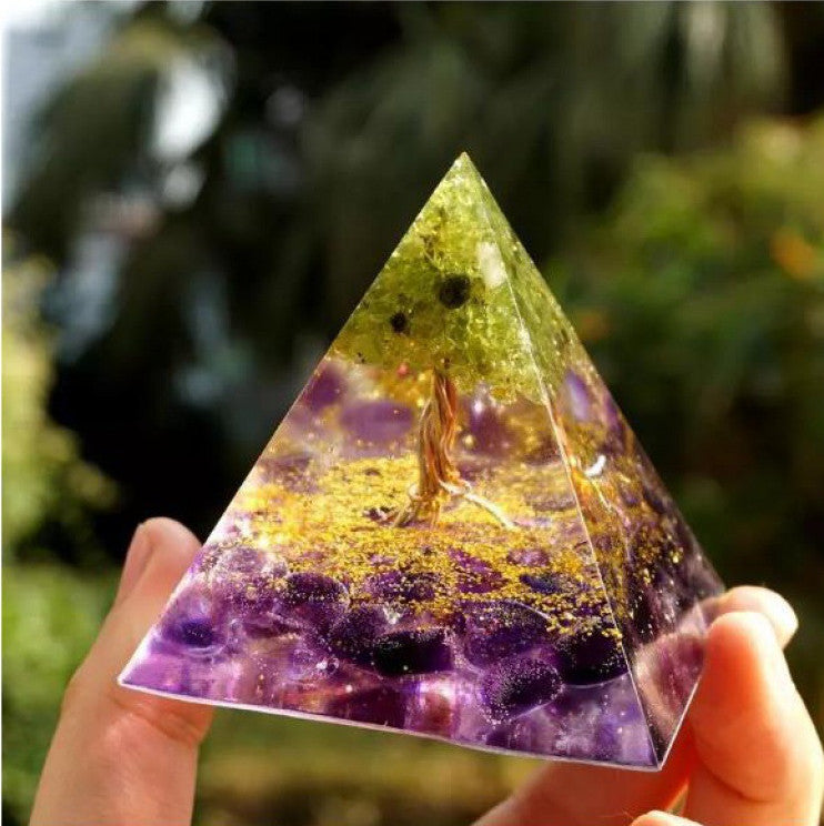 Triangular crystal pyramid held by a hand with a blurred natural background