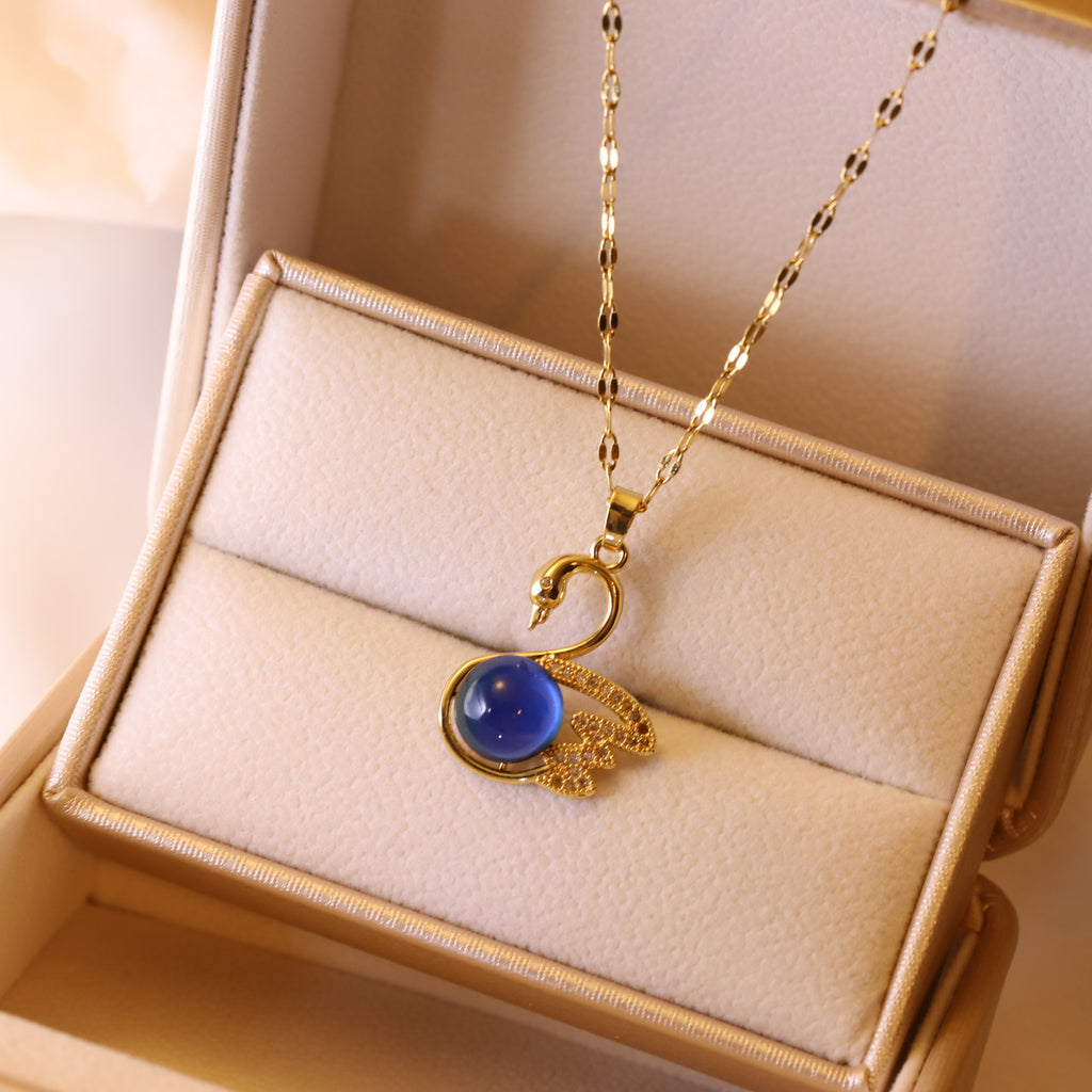 Gold necklace with a blue pendant on a beige jewelry display box.