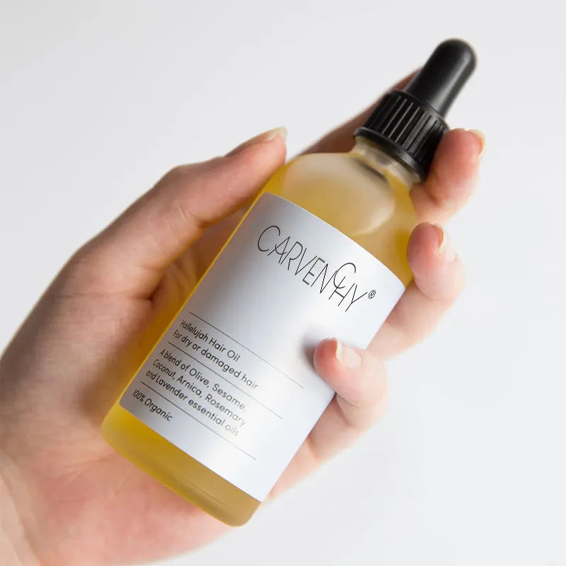 Hand holding a bottle of Carvenny hair oil with a white label on a light gray background