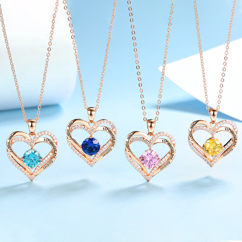 Four heart-shaped pendants with colored stones on rose gold chains against a light blue background.