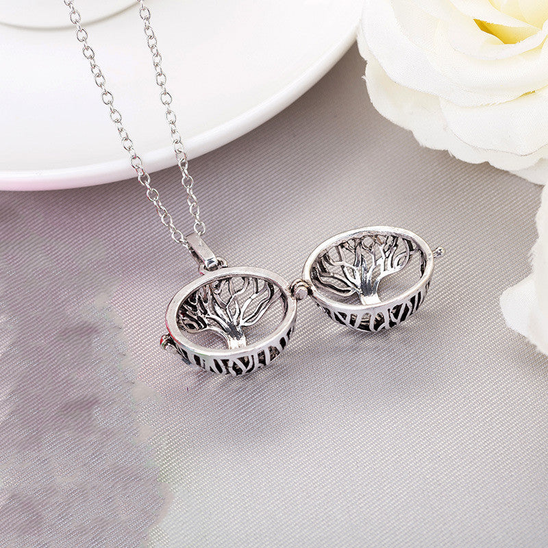 Silver tree-shaped locket necklace on a light gray surface with white flowers in the background.