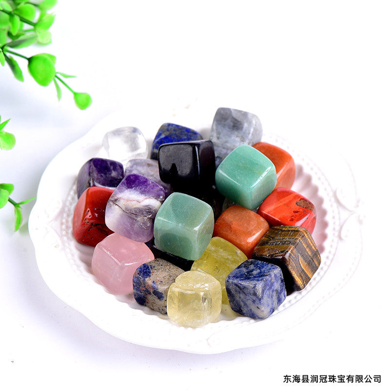Assorted colorful gemstones on a white plate with green leaves in the background