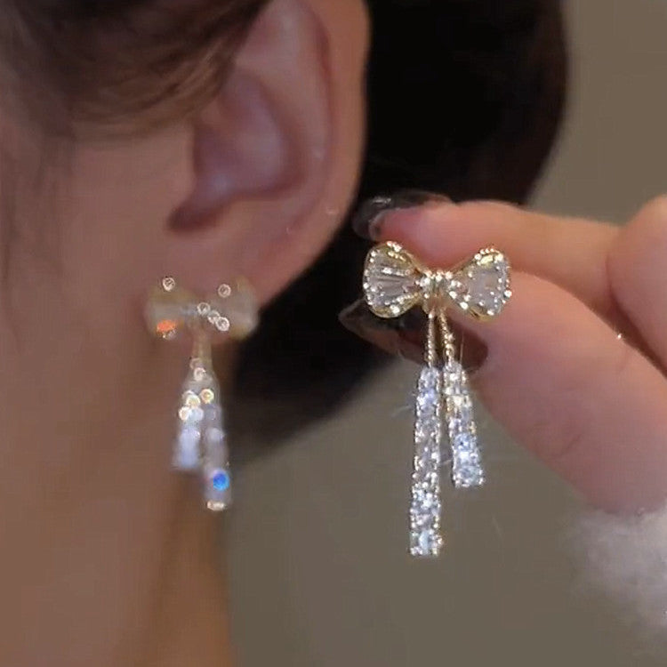 Close-up of a person wearing bow-shaped earrings with tassels.