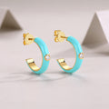 Turquoise hoop earrings with gold accents on a light gray background