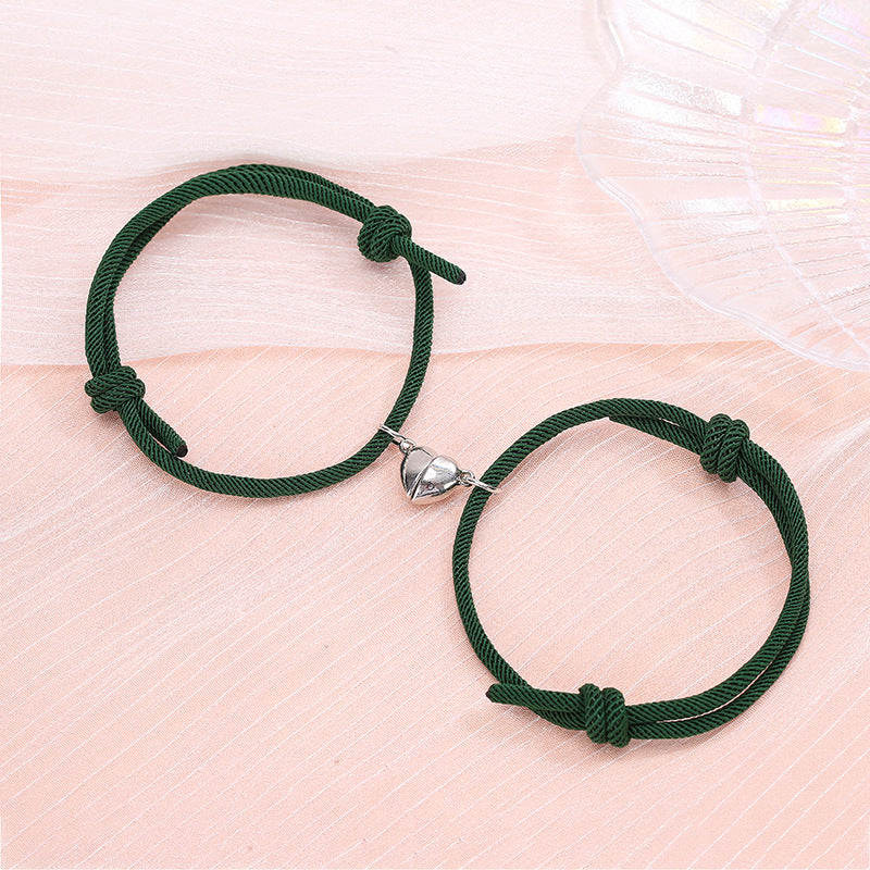 Two green bracelets with silver heart charms on a light pink surface