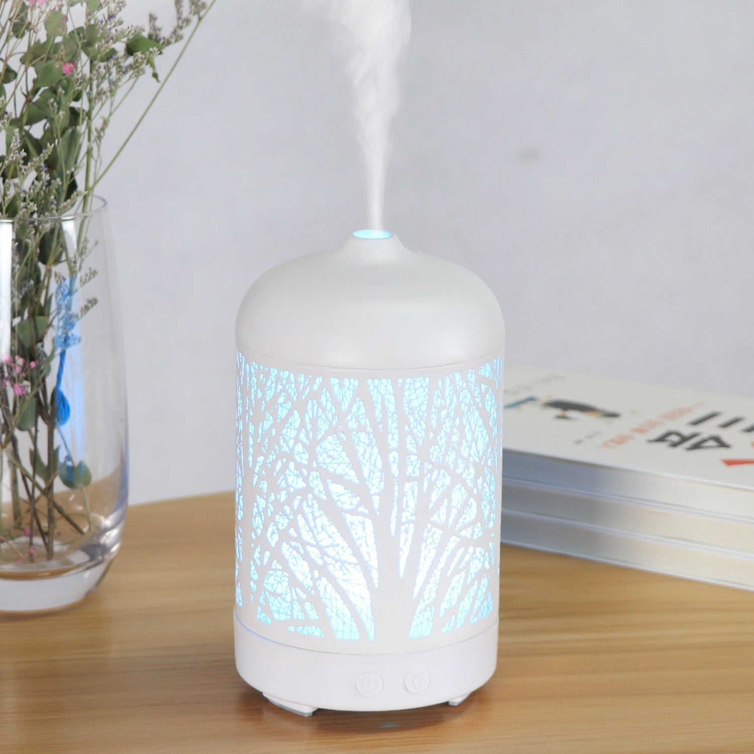 White diffuser emitting mist on a wooden surface with a vase of flowers and books in the background