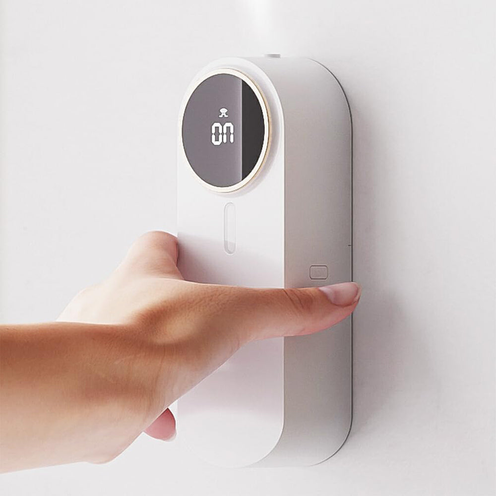 Hand pressing a white wall-mounted device with a digital display on a light gray background
