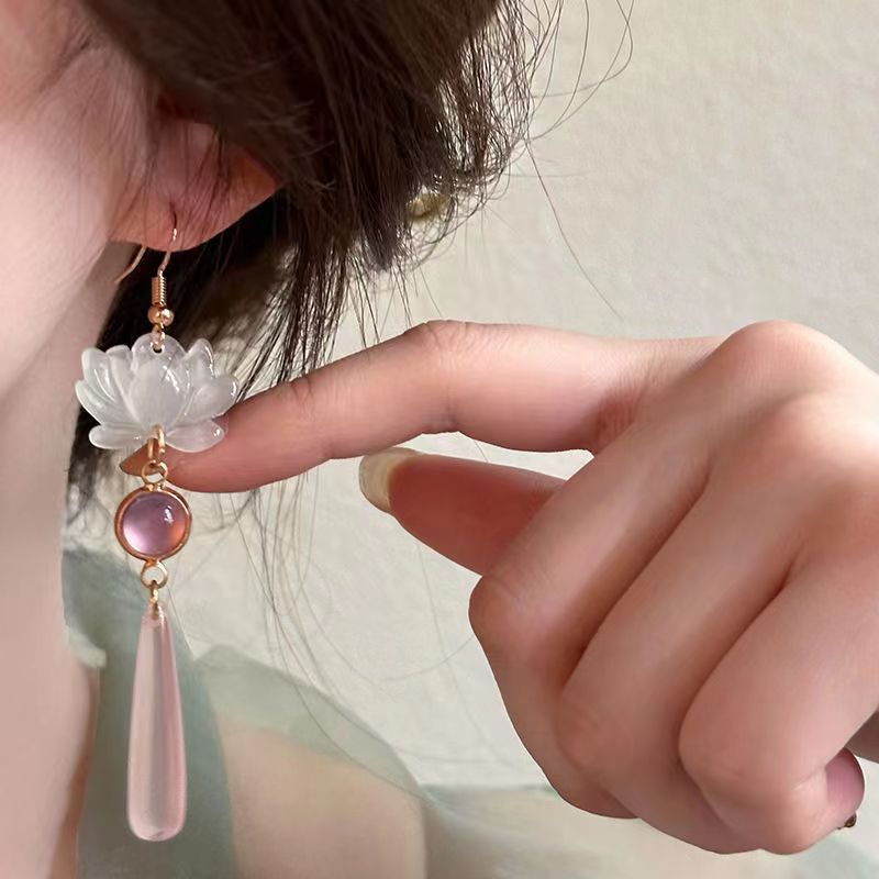 Close-up of a hand wearing a floral earring with pink and clear stones.