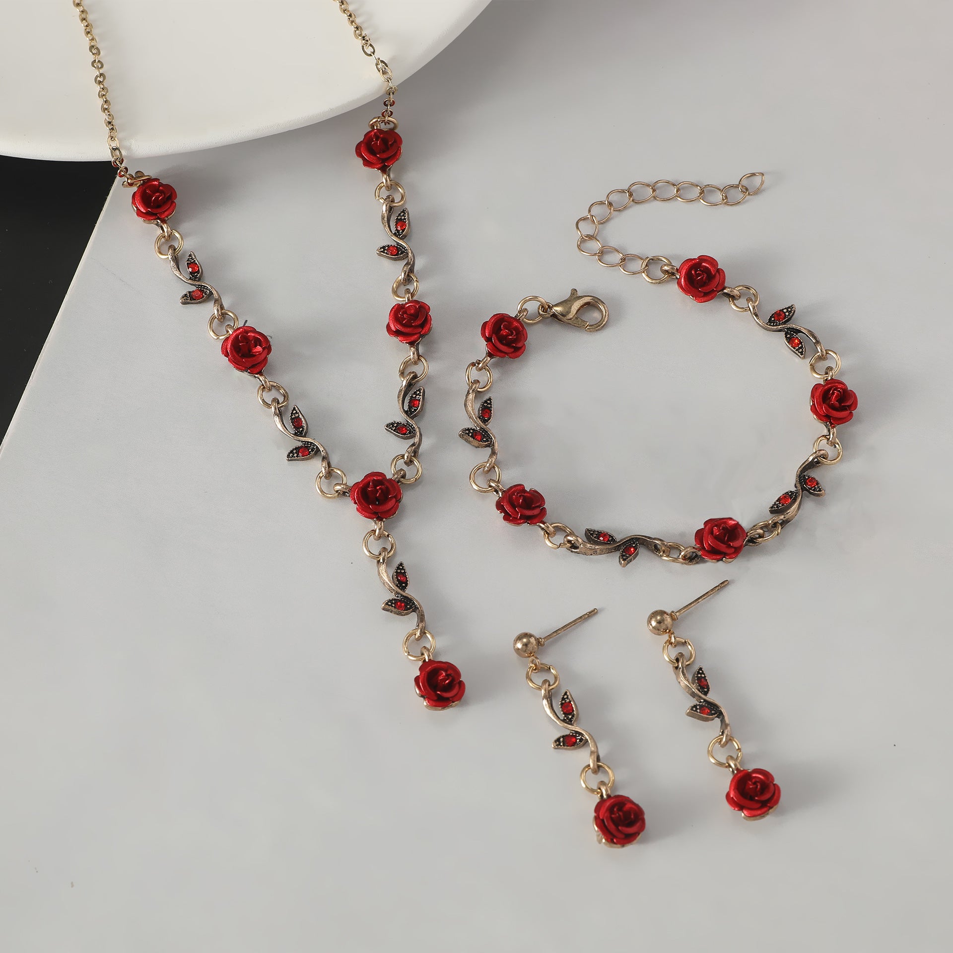 Jewelry set with red rose details on a white surface