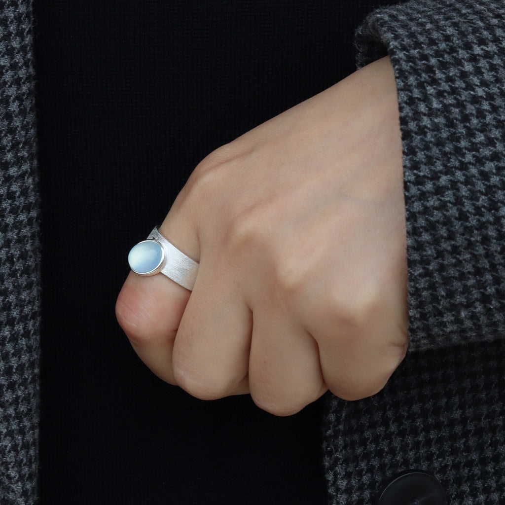 Hand wearing a silver ring with a dark coat background