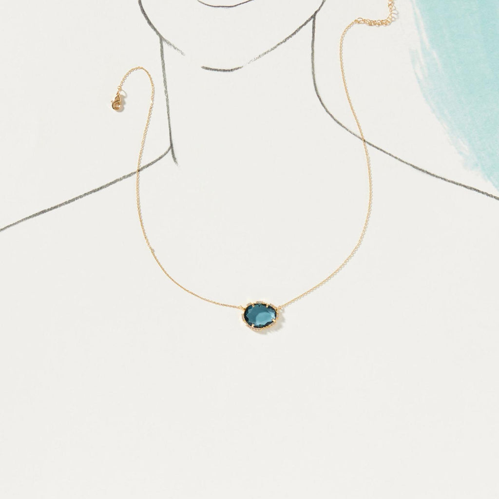 Gold necklace with a blue pendant on a light background