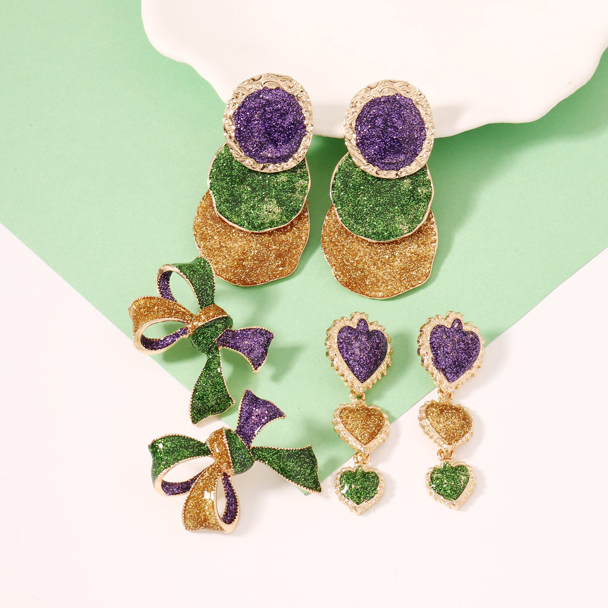 Colorful earrings with green, purple, and gold colors on a light green background