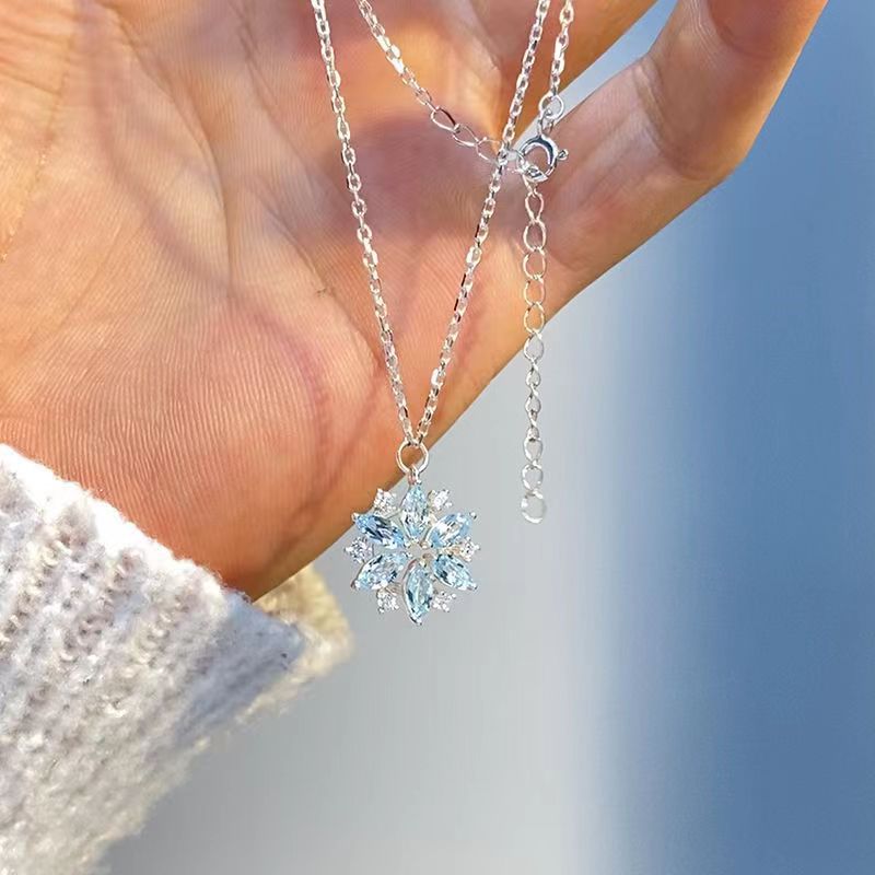 Silver necklace with a snowflake pendant held by a hand against a blurred natural background