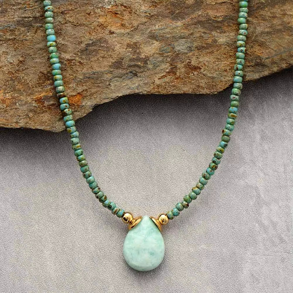 Turquoise beaded necklace with a gold accent and green pendant on a stone background