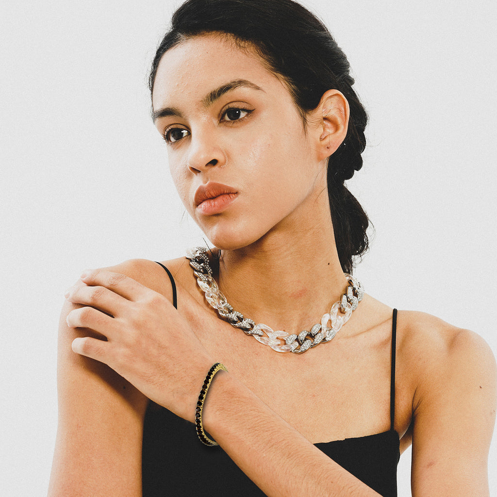 Woman wearing a black top and layered necklaces on a plain background