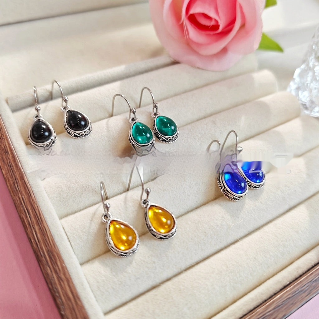 Set of colorful teardrop-shaped earrings on a jewelry display with a pink rose in the background.