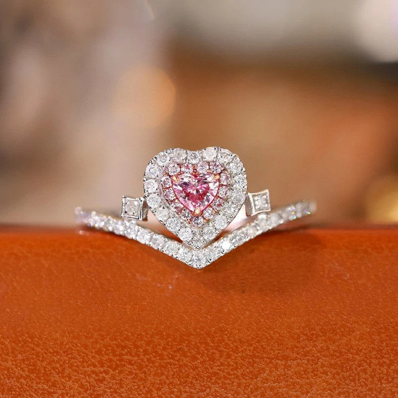 Heart-shaped pink gemstone ring with diamond accents on an orange surface