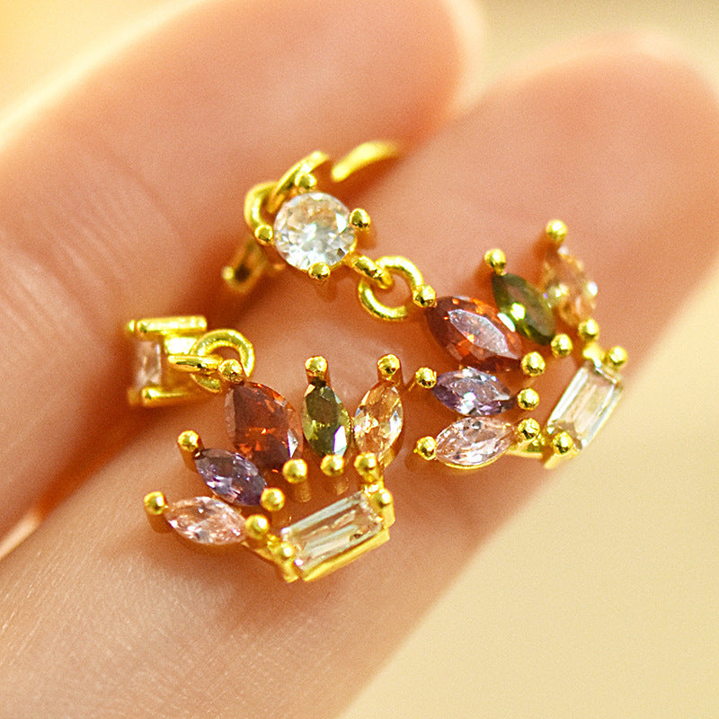 Gold earrings with multicolored gemstones held on a hand against a beige background