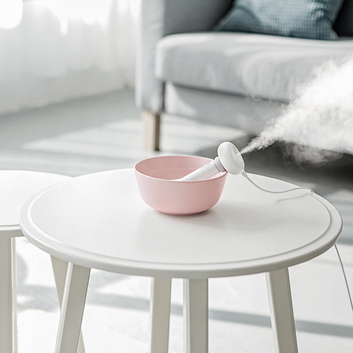 Pink humidifier on a white table with steam rising, blurred background