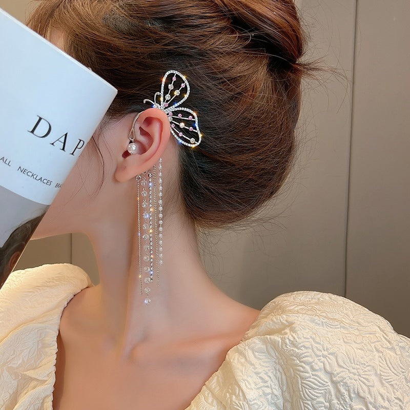Close-up of a woman's ear with a decorative earring, hairpin, and pearl, with a neutral background.