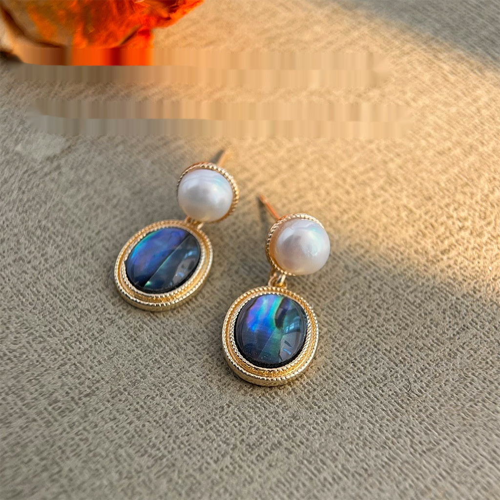 Pair of earrings with pearl and abalone shell design on a textured surface