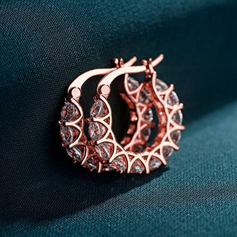 Rose gold hoop earrings with gemstones on a dark fabric background