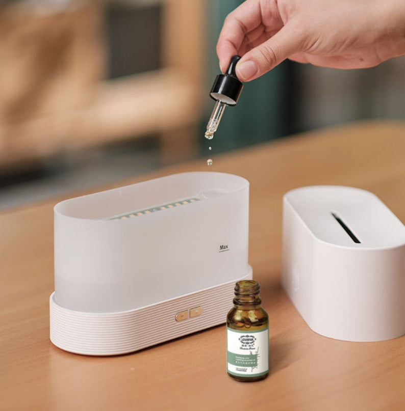 Hand using a dropper to add liquid into a white device on a wooden surface with a bottle of essential oil nearby.
