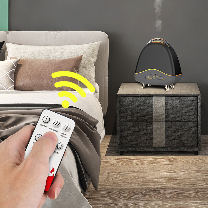 Hand holding a remote control next to a humidifier on a nightstand in a bedroom.