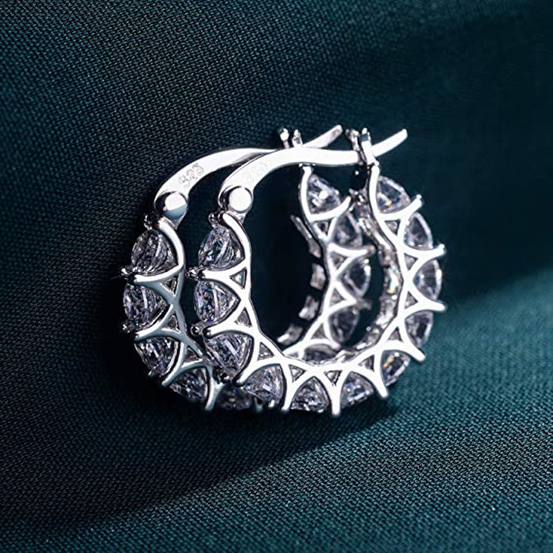Silver hoop earrings with intricate designs on a dark fabric background