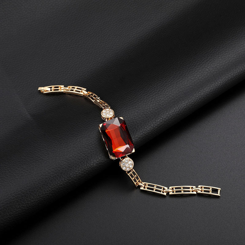 Gold bracelet with a red gemstone on a black fabric background