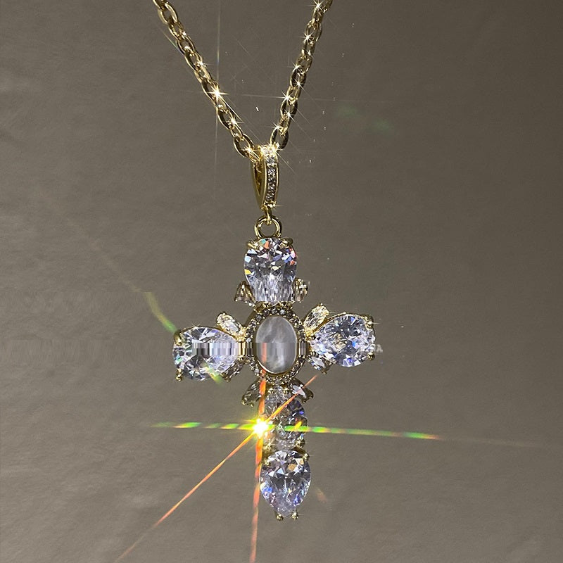 Gold cross pendant with gemstones on a chain against a gray background