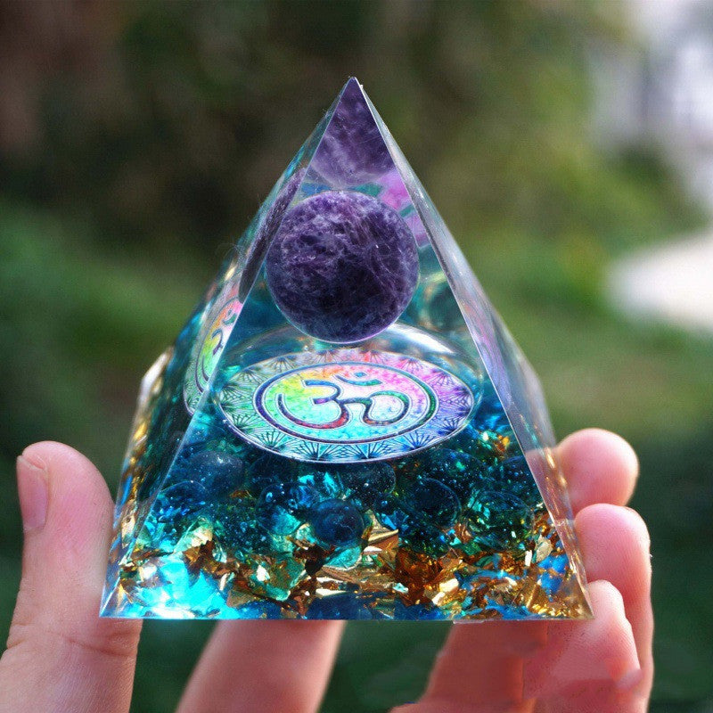 Triangular crystal pyramid with purple sphere and Om symbol held by a hand against a blurred green background