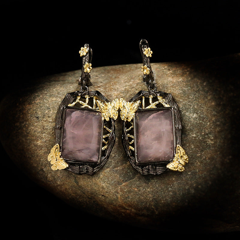 Pair of earrings with purple stones and gold butterfly accents on a dark background