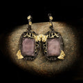 Pair of earrings with purple stones and gold butterfly accents on a dark background