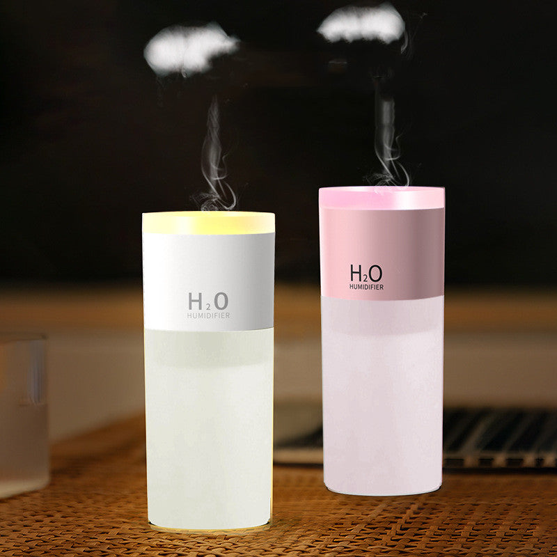 Two H2O humidifiers, one white and one pink, emitting steam on a wooden surface.