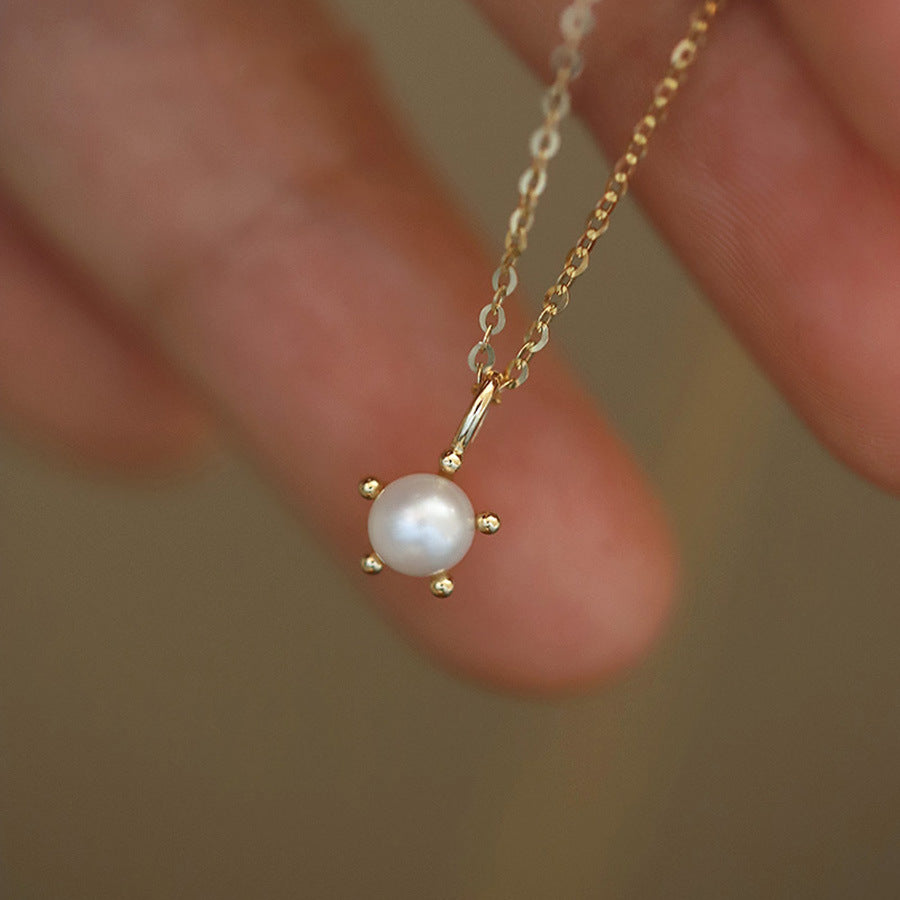 Delicate gold necklace with a pearl pendant held between fingers against a blurred background