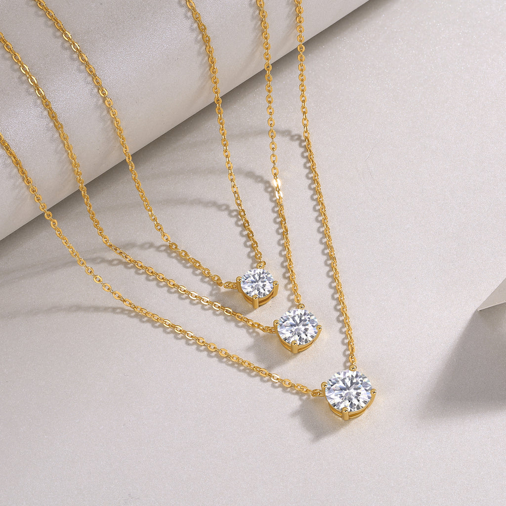 Gold necklaces with diamond pendants on a light gray background
