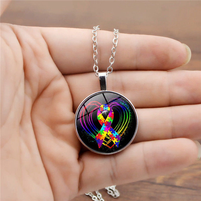Necklace with a colorful heart and ribbon pendant held in a hand.